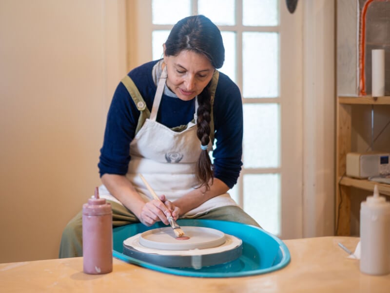 A woman sitting at a pottery wheel is demonstrating pottery painting techniques